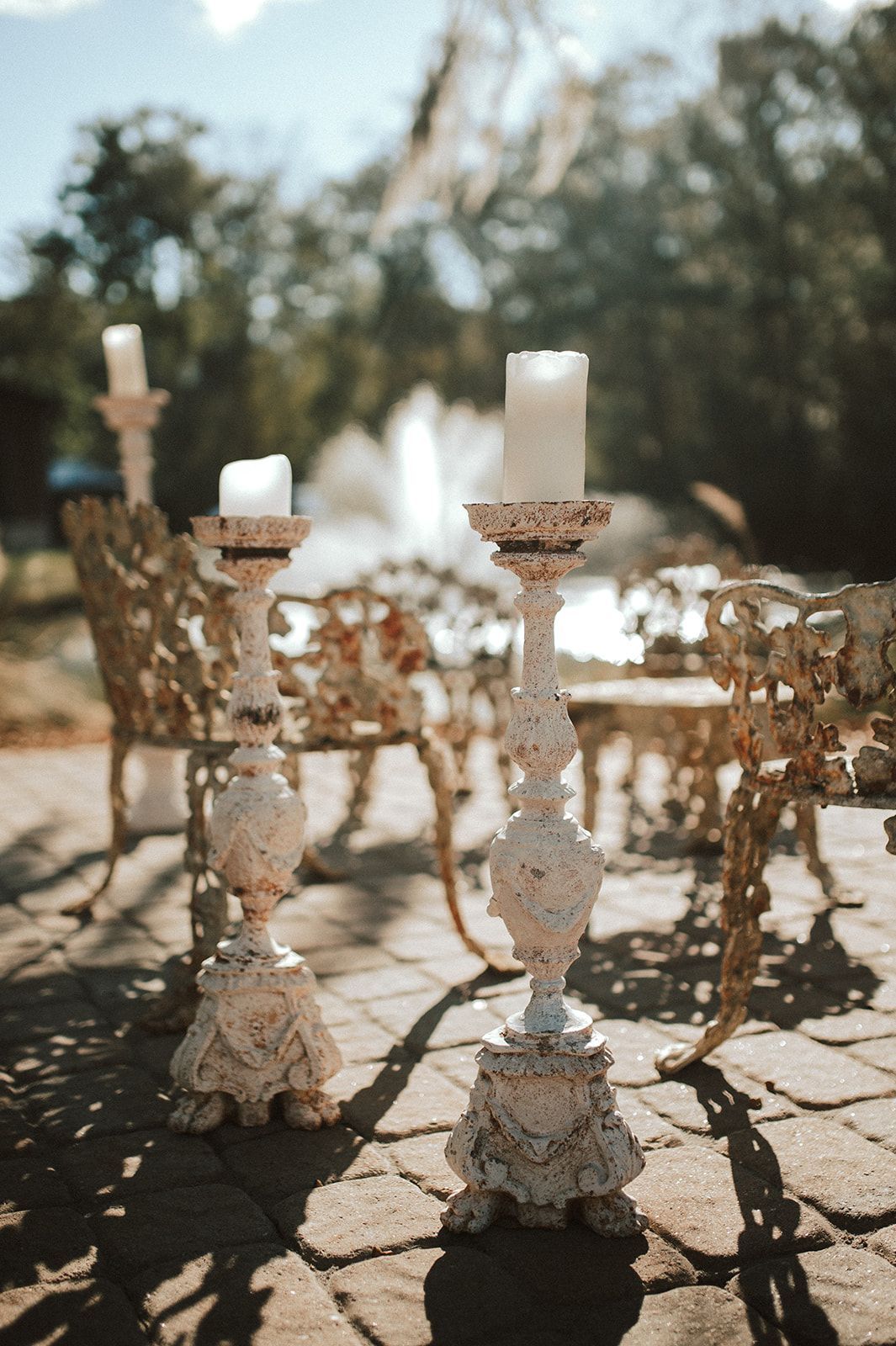 Decorative candleholders on an outdoor patio with a fountain and blurred trees in the background
