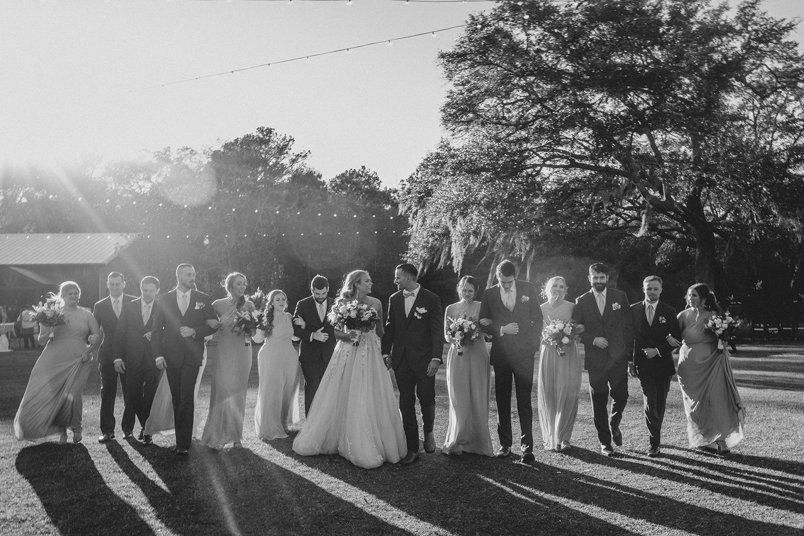 Wedding party posing outdoors at sunset, with the bride in a white gown and others in formal attire