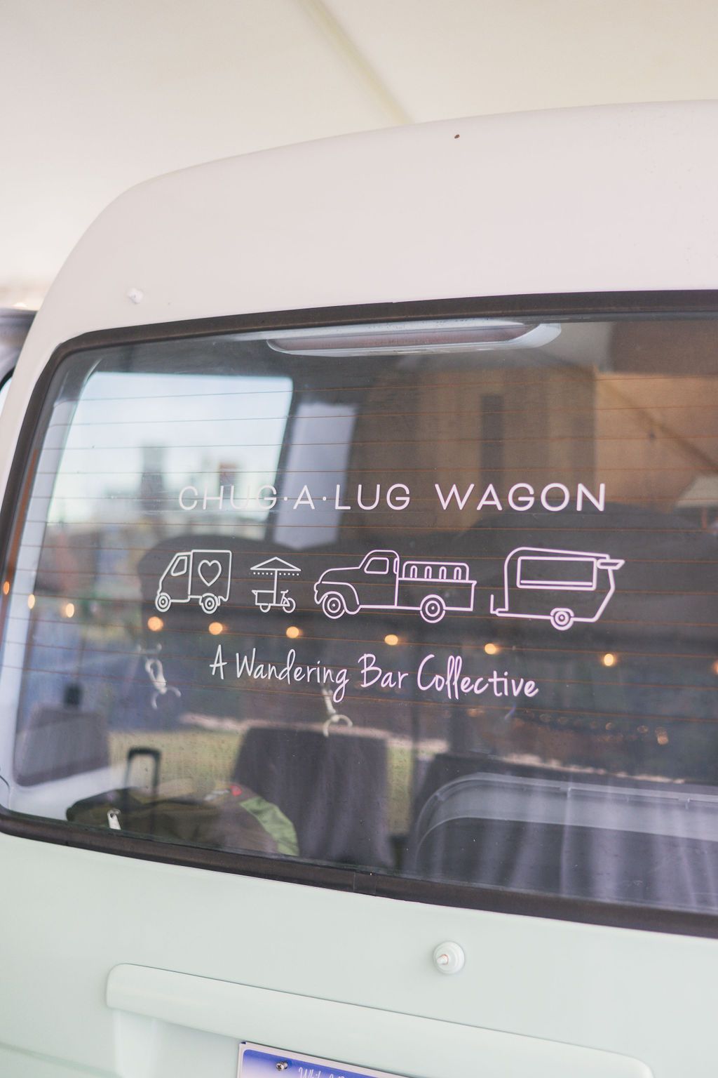 Rear window of a white van with “LUX WAGON” and pictogram decals advertising a luxury transport service