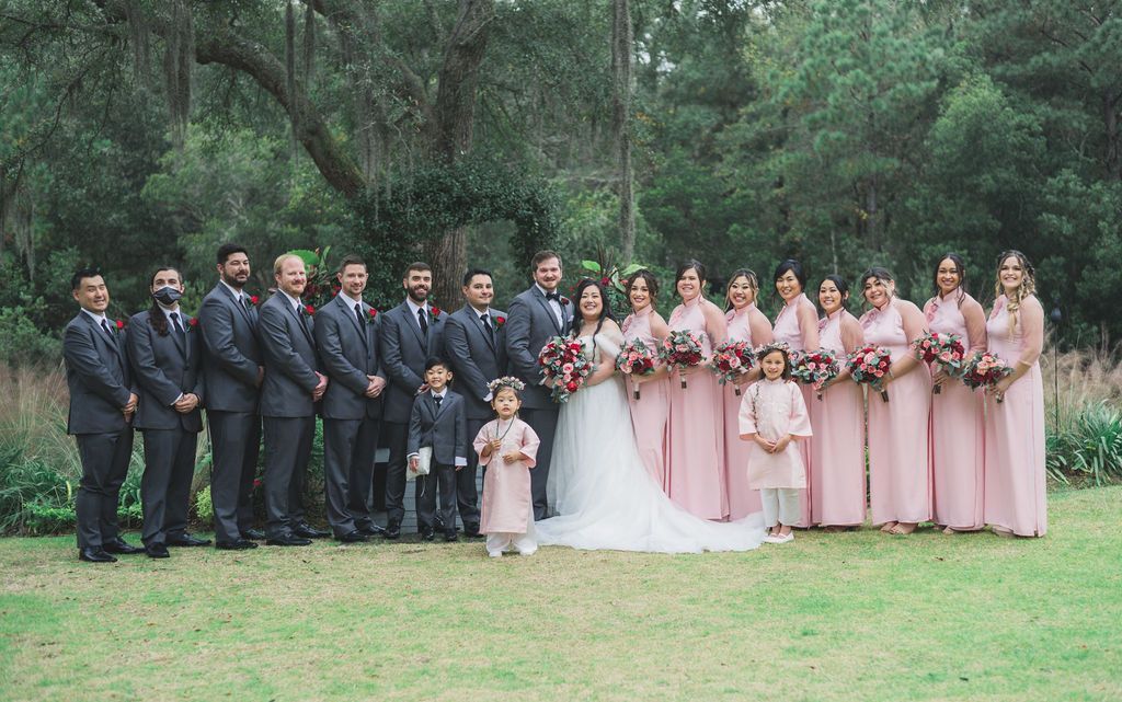 Wedding party posing outdoors, with bride in white and bridesmaids in pink beside groomsmen in dark suits