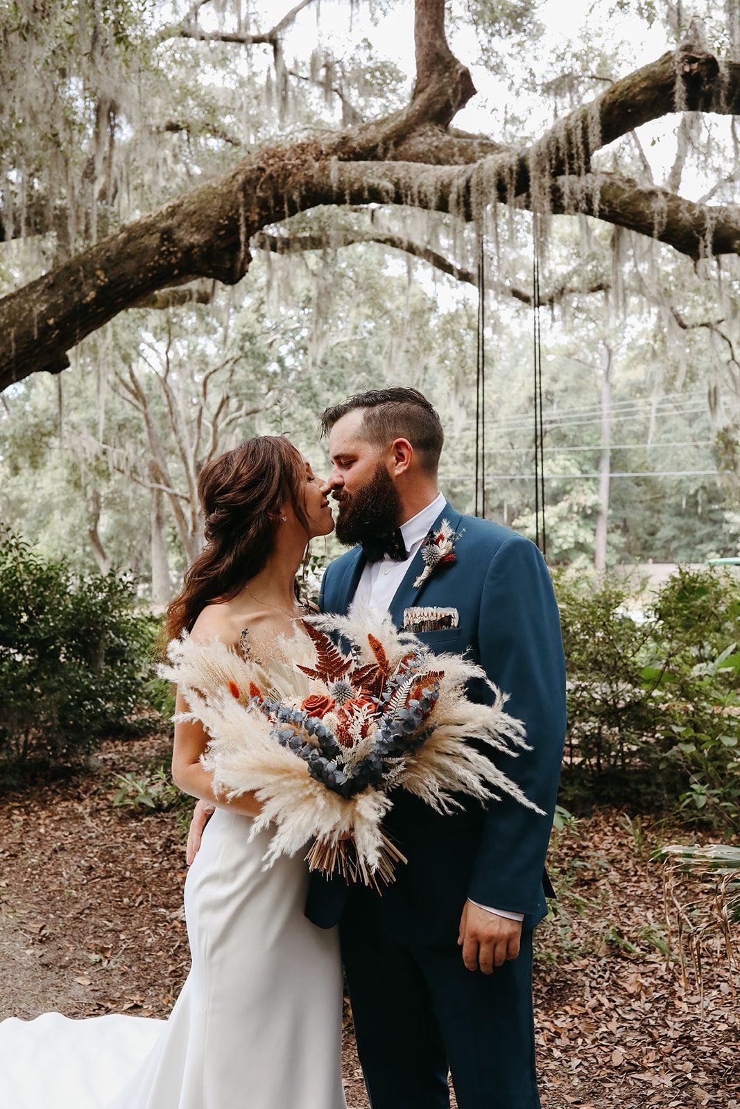 Couple embracing under a large tree, the bride holding a bouquet in an outdoor garden setting.