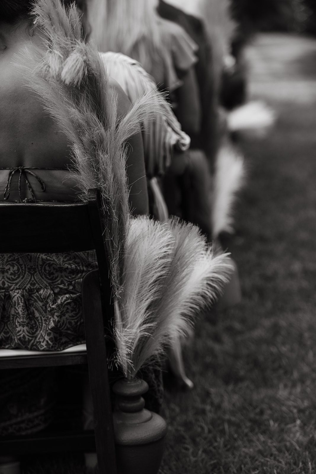 Black and white close-up of decorative feathers in vases along a grassy outdoor aisle.
