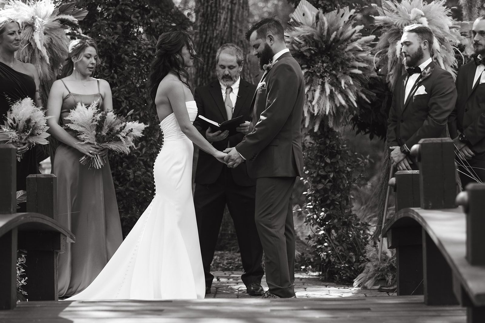 Wedding couple exchanging vows at an outdoor garden ceremony, with attendants standing nearby