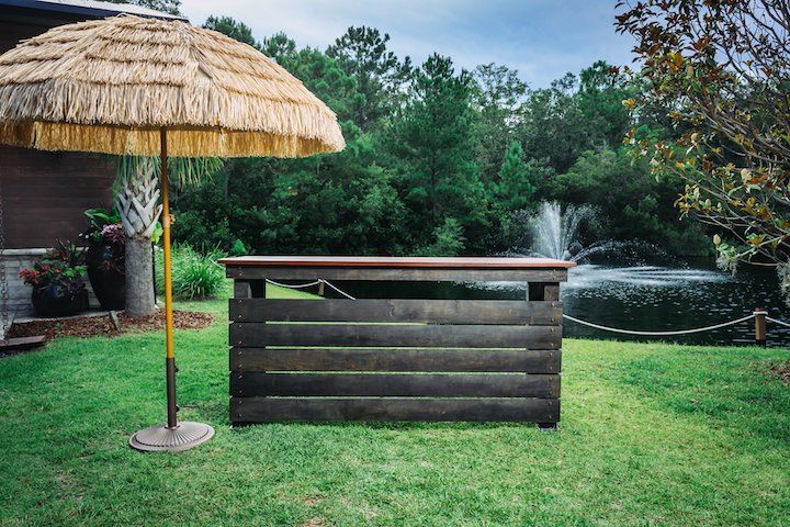 Backyard tiki bar with a thatched umbrella and a hot tub in the background