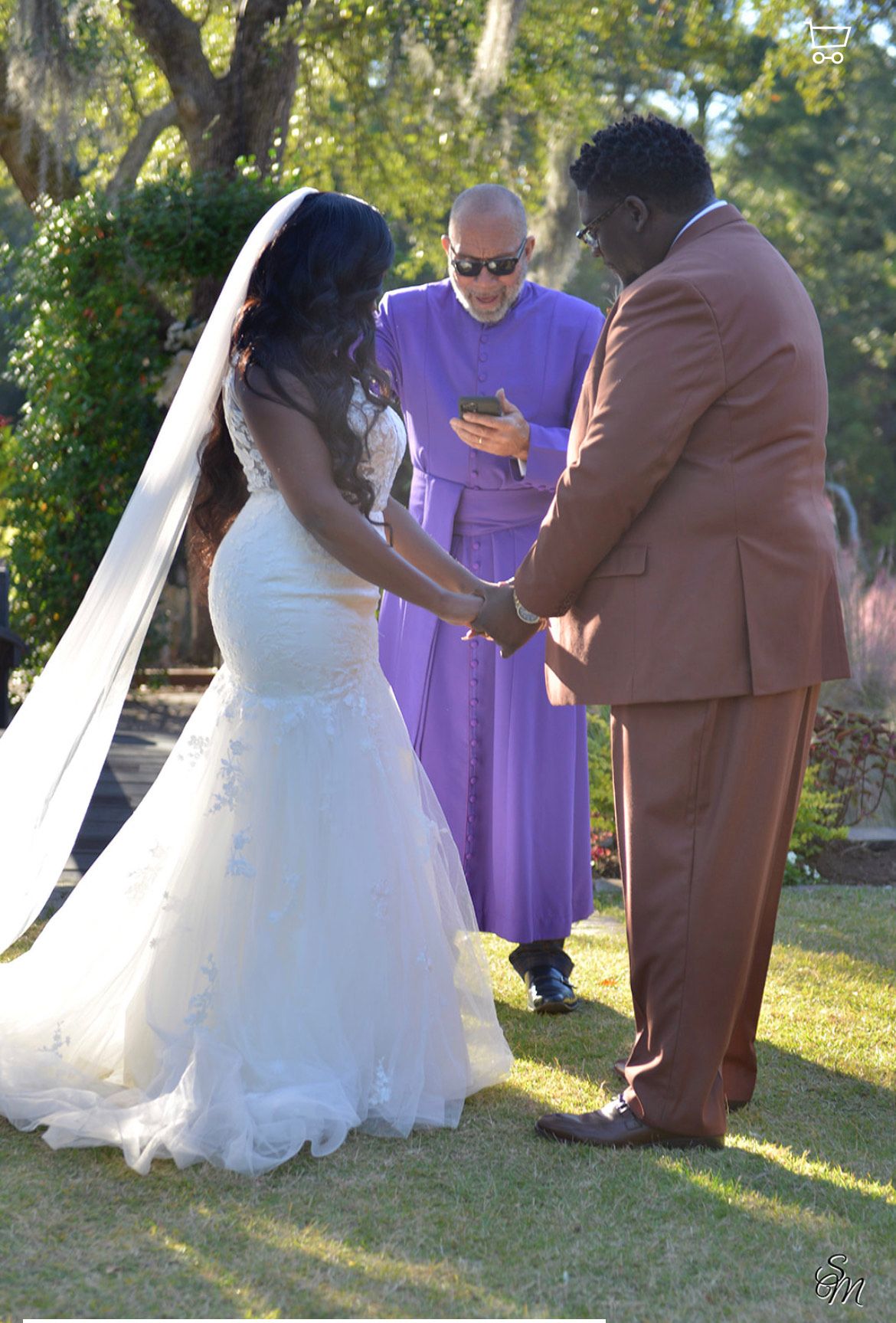 Bride and groom hold hands during an outdoor wedding ceremony, with officiant in purple standing between them.