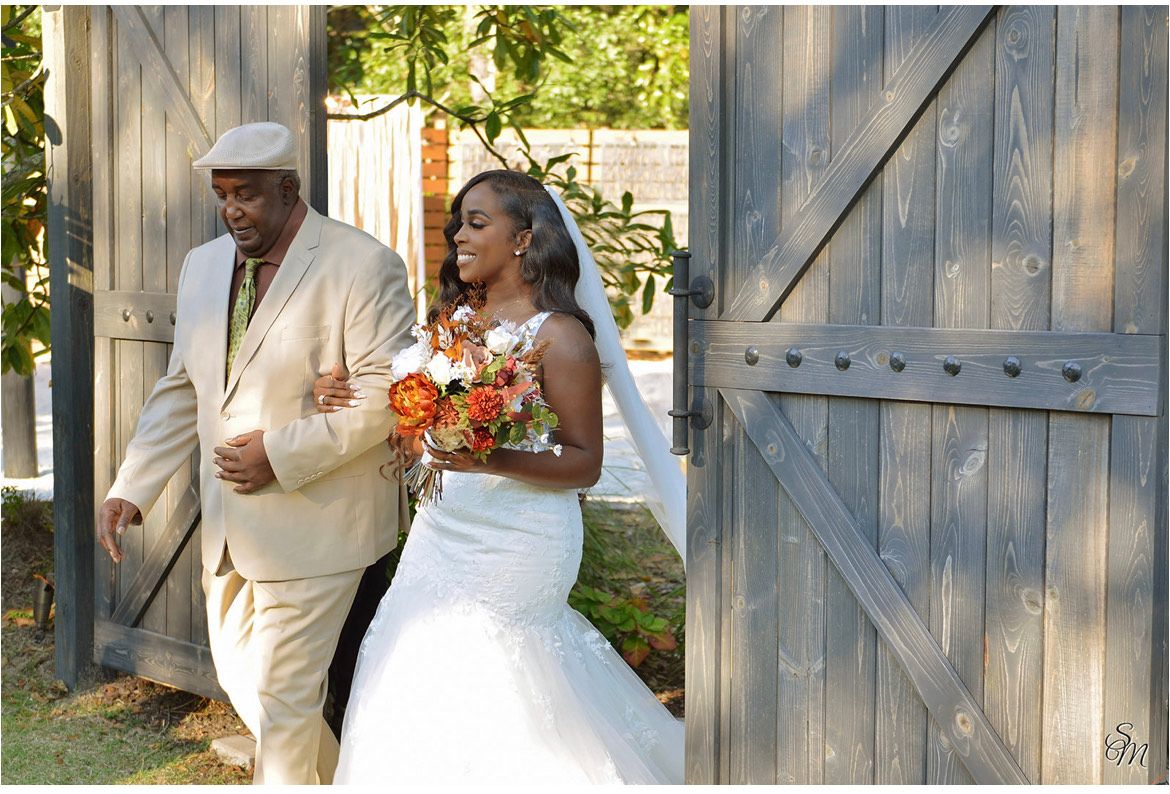Bride and groom walking by a wooden gate, bride holding a colorful bouquet