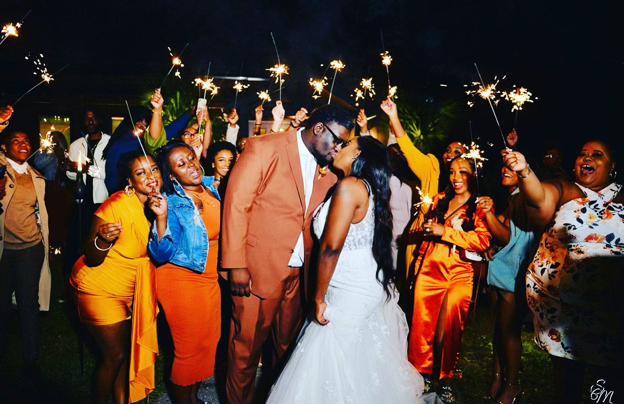 Bride and groom kiss amid cheering guests holding sparklers at a nighttime celebration