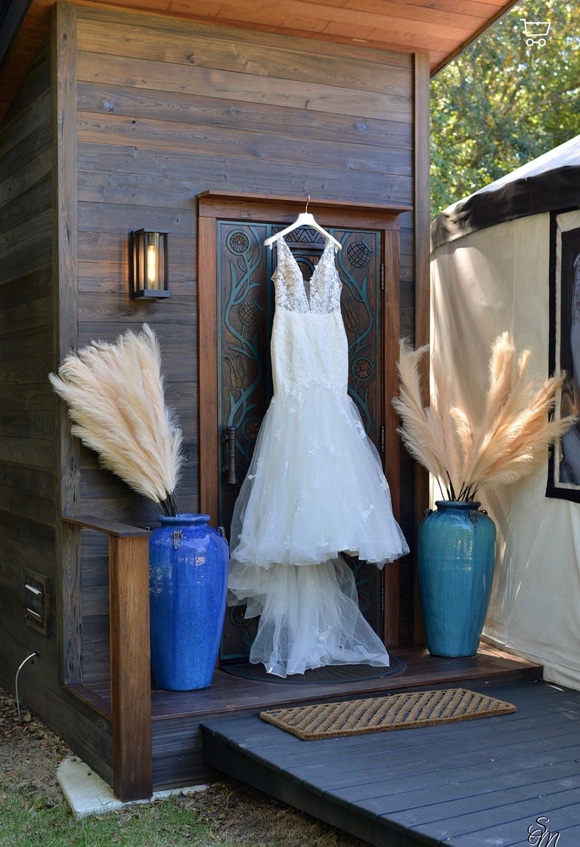 White wedding dress hanging in rustic outdoor display with blue and tan vases and pampas grass