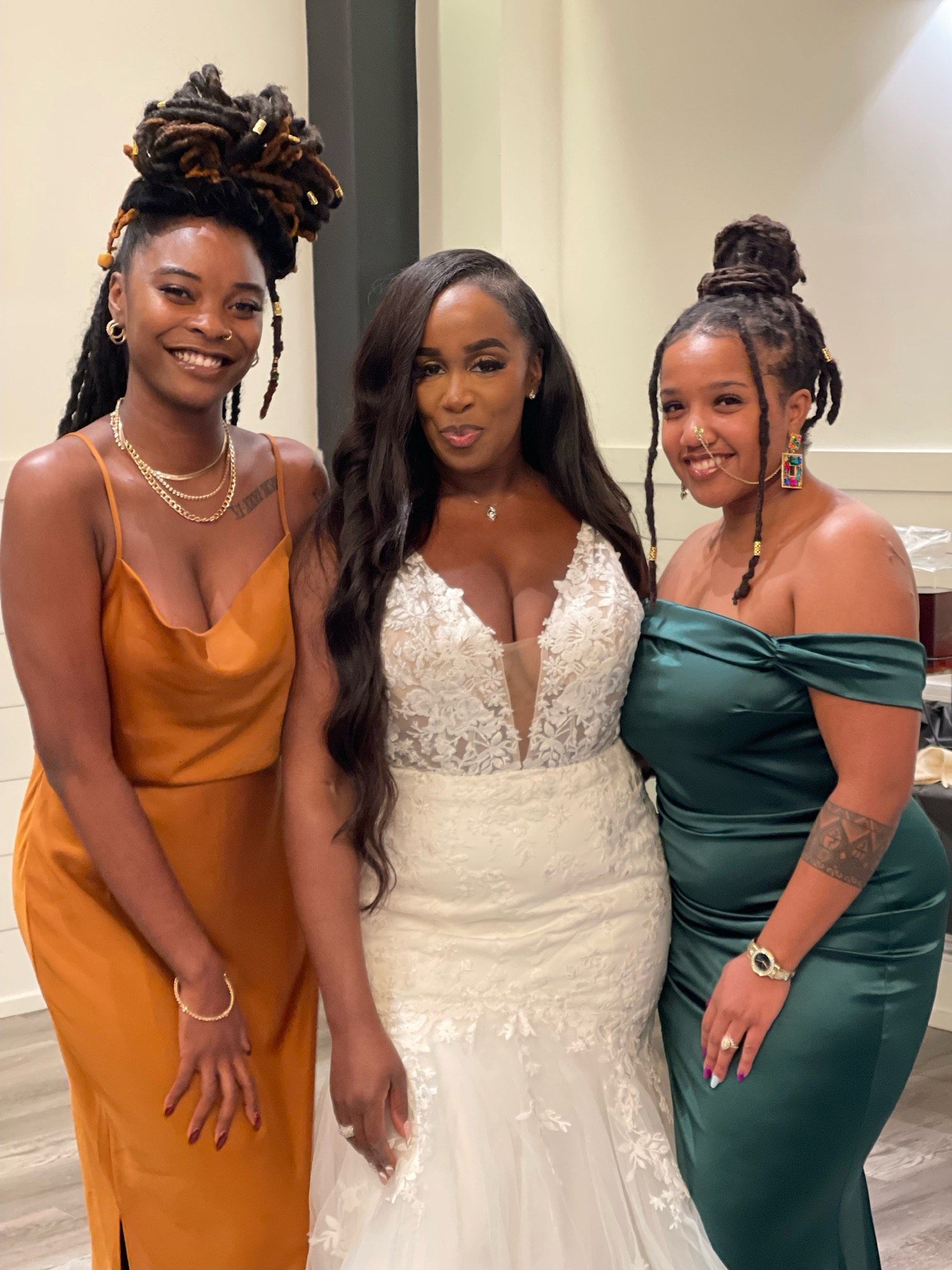 Three women posing in formal dresses, smiling indoors at a celebration.