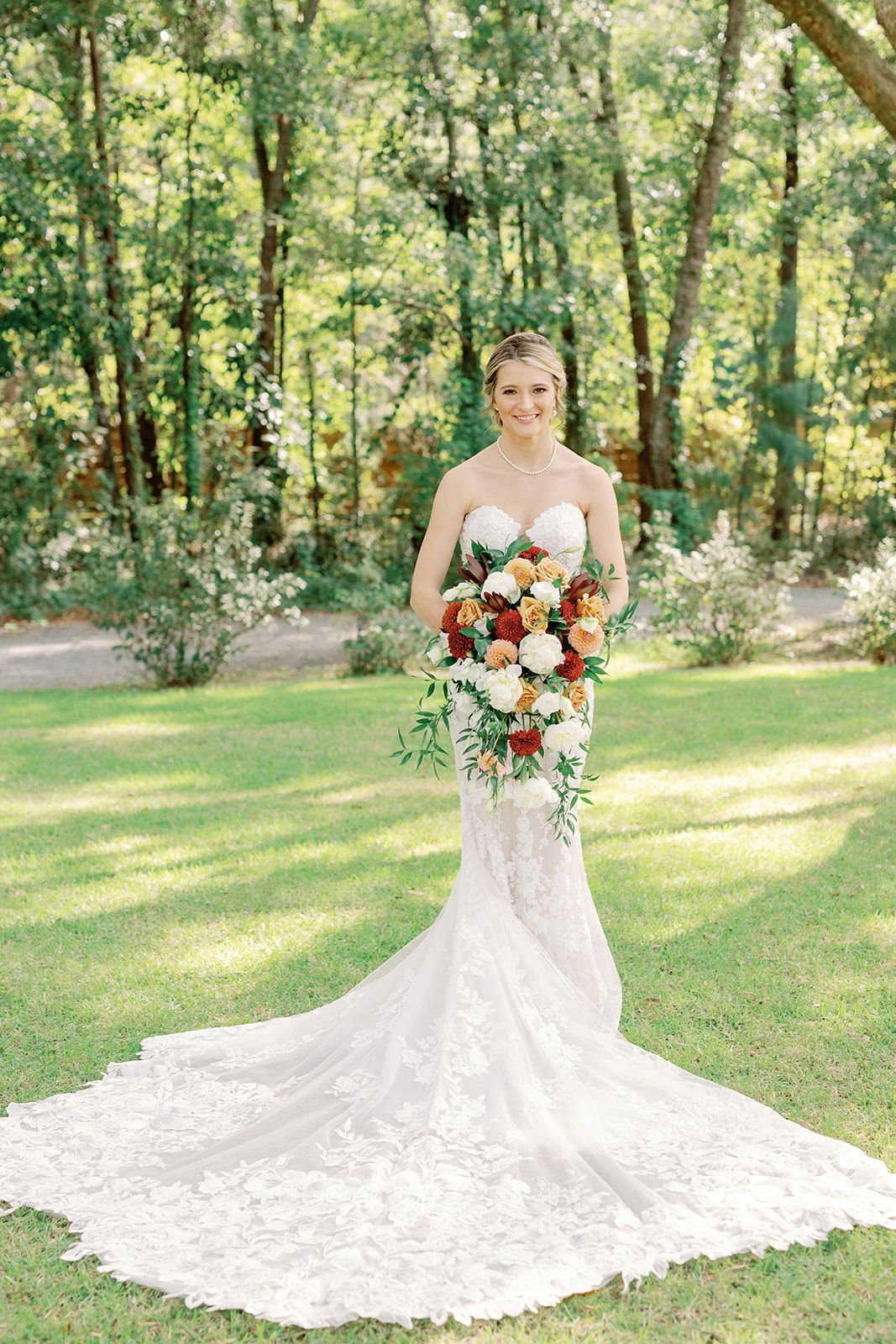 Bride in a white lace gown holding a colorful bouquet in a sunlit garden
