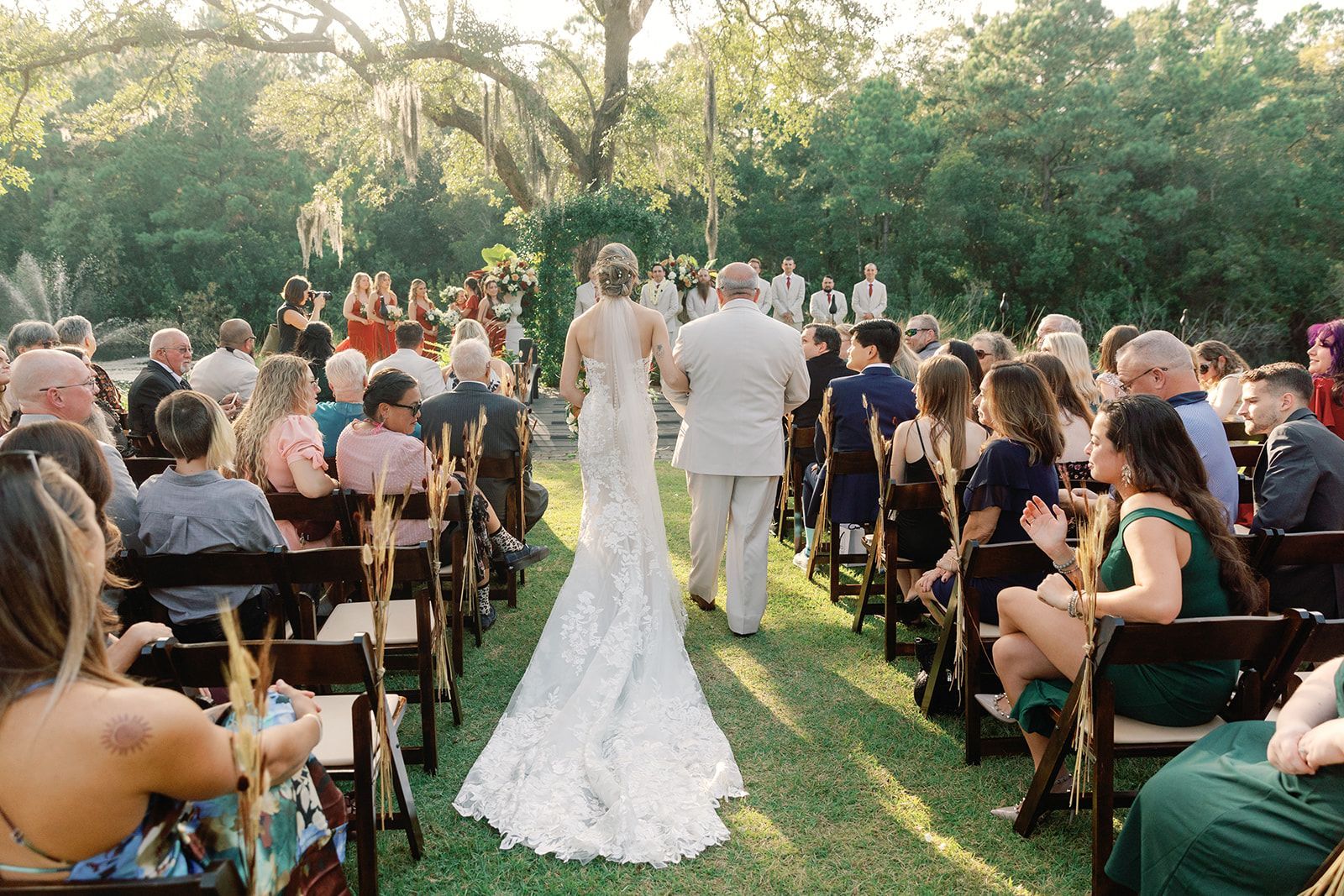 Outdoor wedding ceremony with bride and groom walking up grassy aisle between seated guests