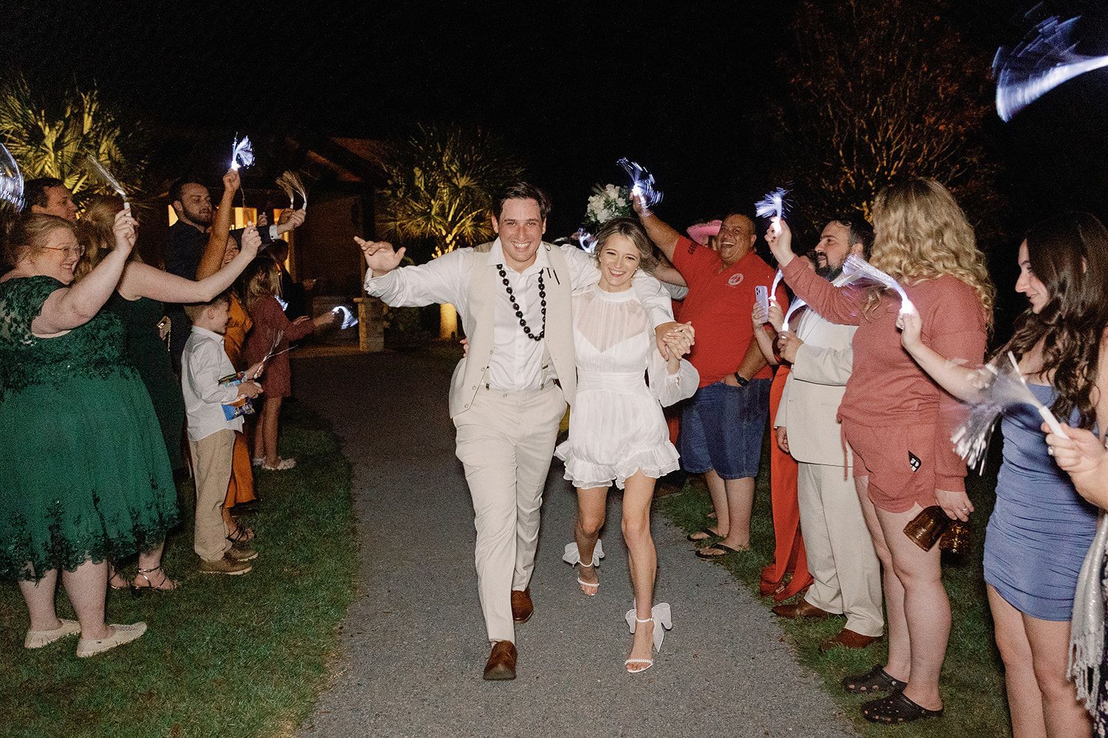 Newlyweds walk through a sparkler send-off tunnel as guests cheer on a garden path.