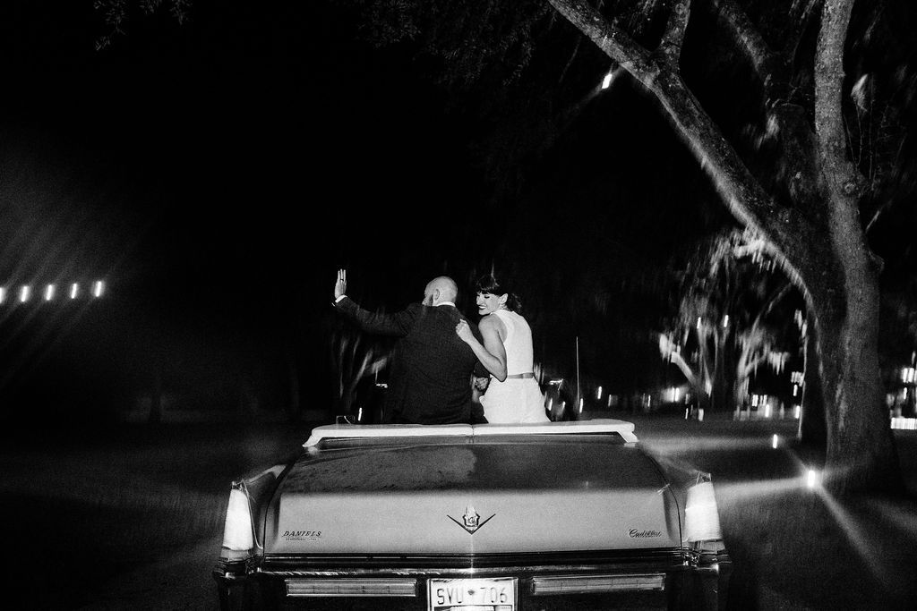 Two people riding in the back of a pickup truck at night on a dark, tree-lined road.