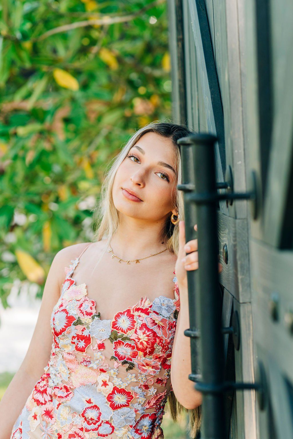 Woman in a floral dress leaning against a train, looking at the camera outdoors.