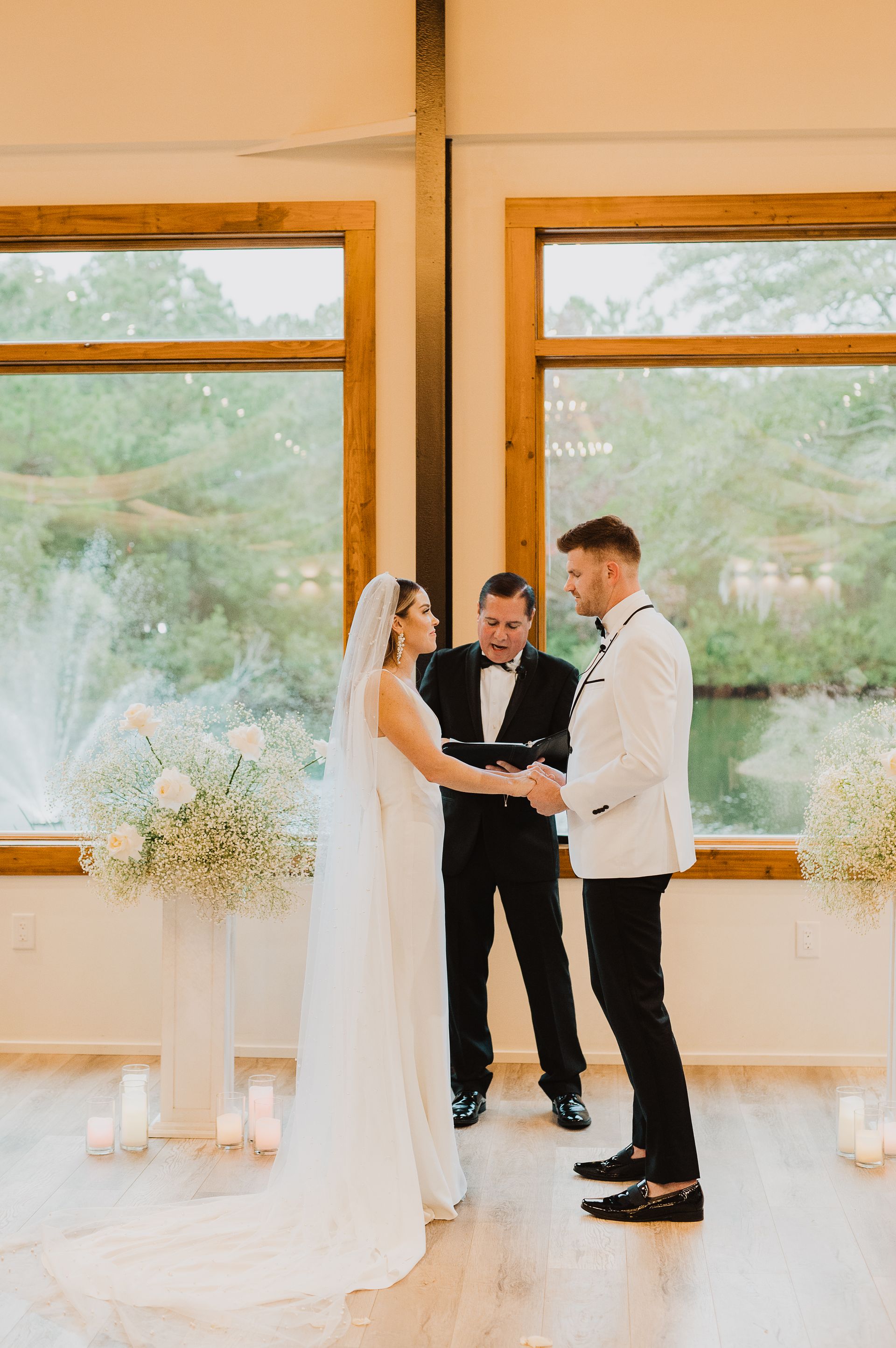 Bride and groom exchanging vows at an indoor wedding ceremony by large windows