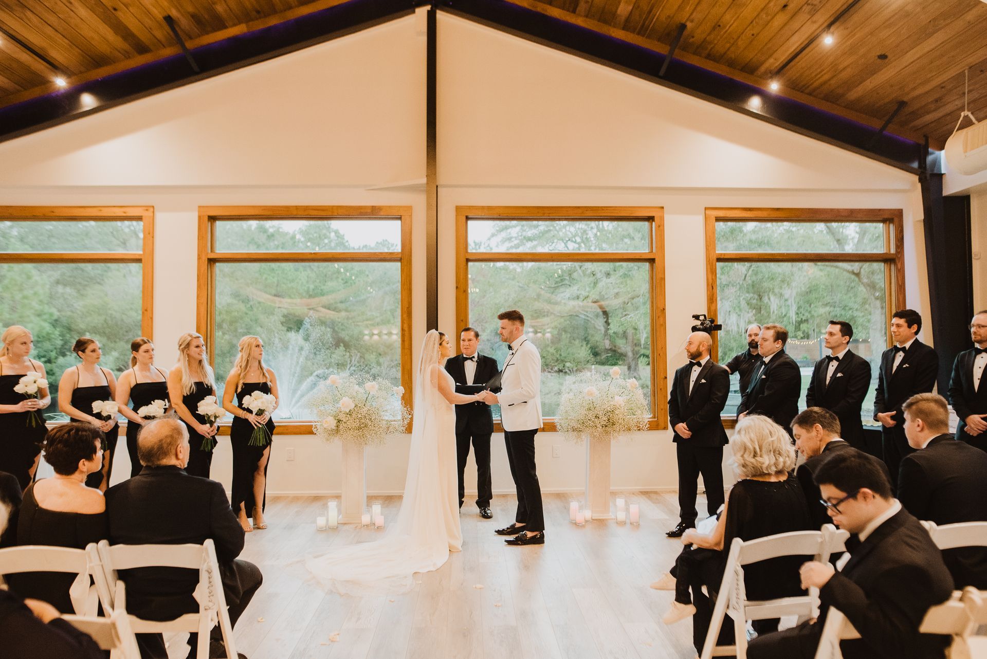 Wedding ceremony in a bright lodge with couple at the altar, guests seated, and attendants standing nearby.
