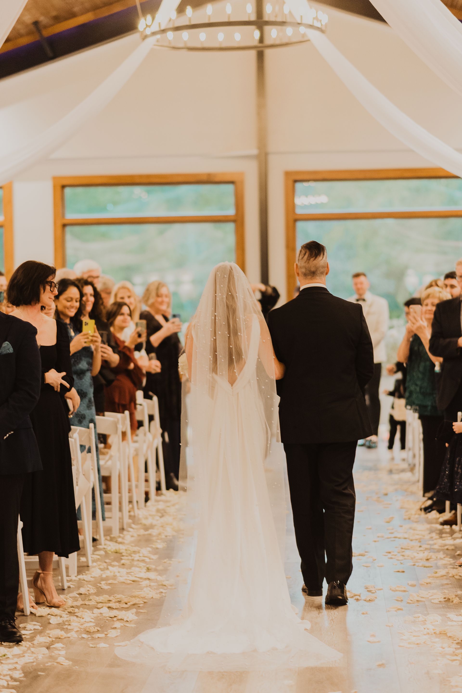 Bride walking down aisle in a bright tented wedding ceremony, guests standing on both sides