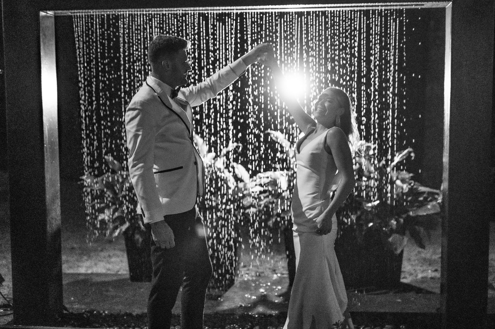 A man and woman dance in front of a sparkling curtain with bright stage lights.
