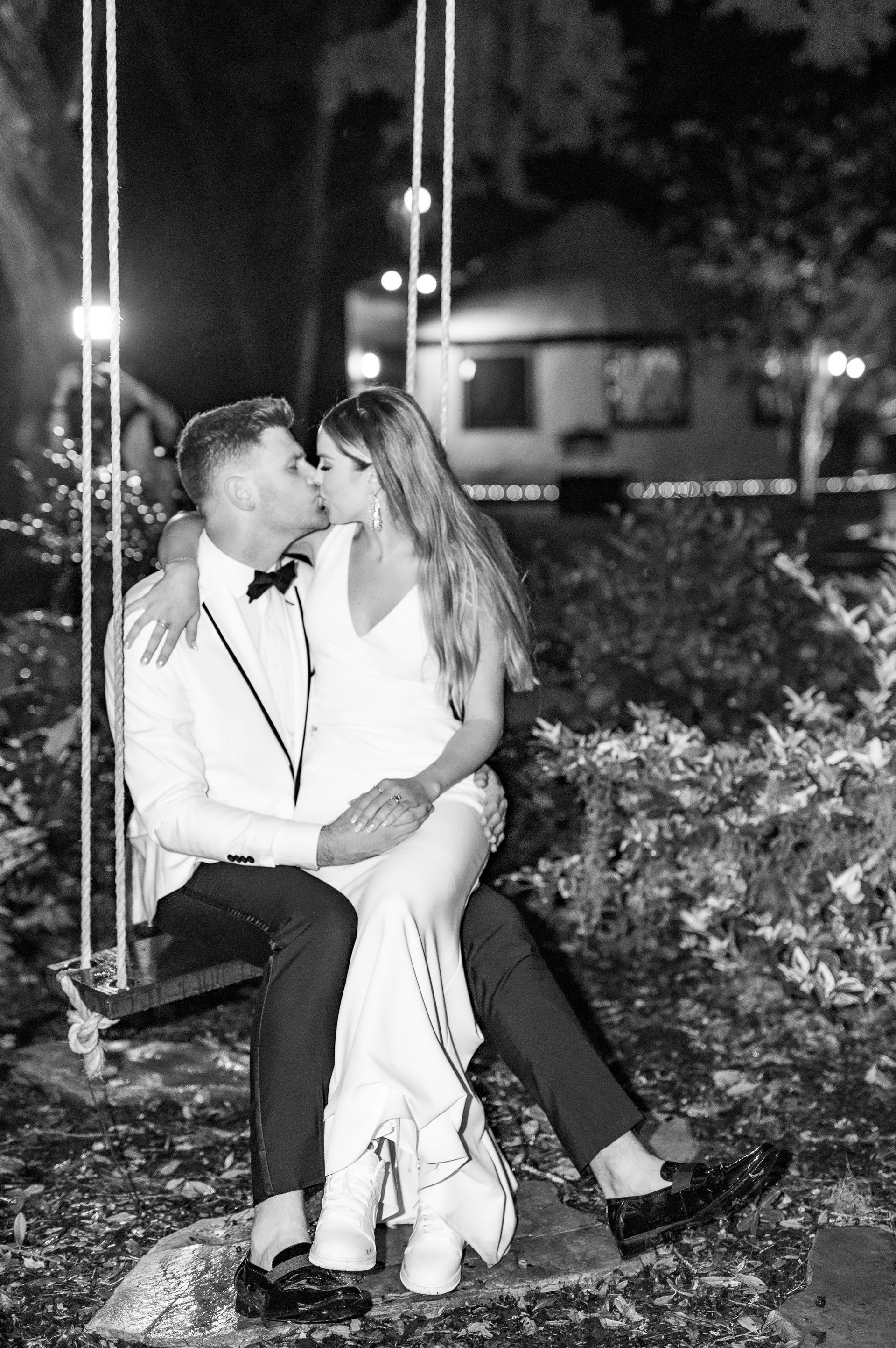 Couple kissing on a garden swing at night, surrounded by lights and greenery