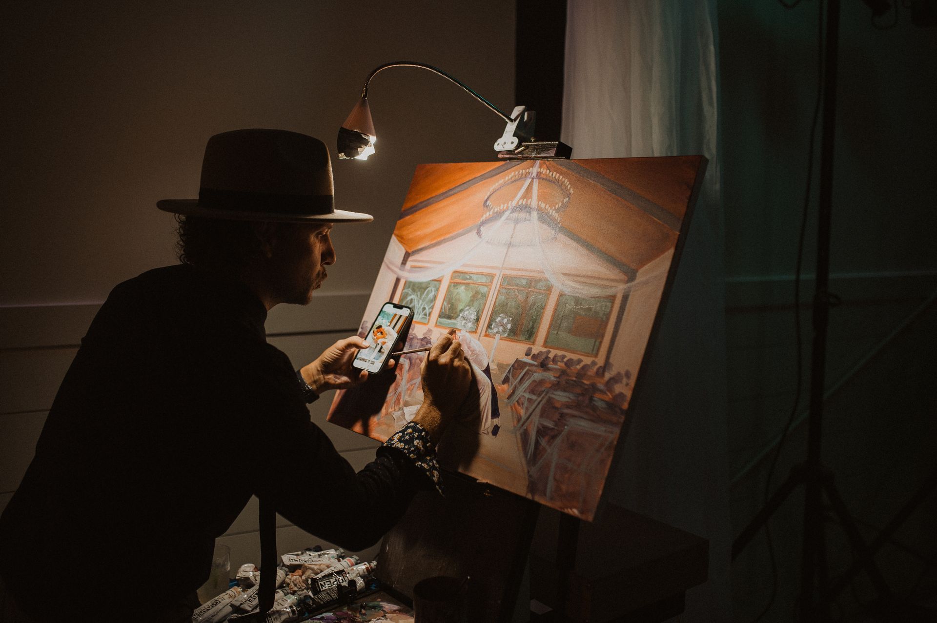 Silhouette of an artist painting a canvas under a lamp in a dim studio