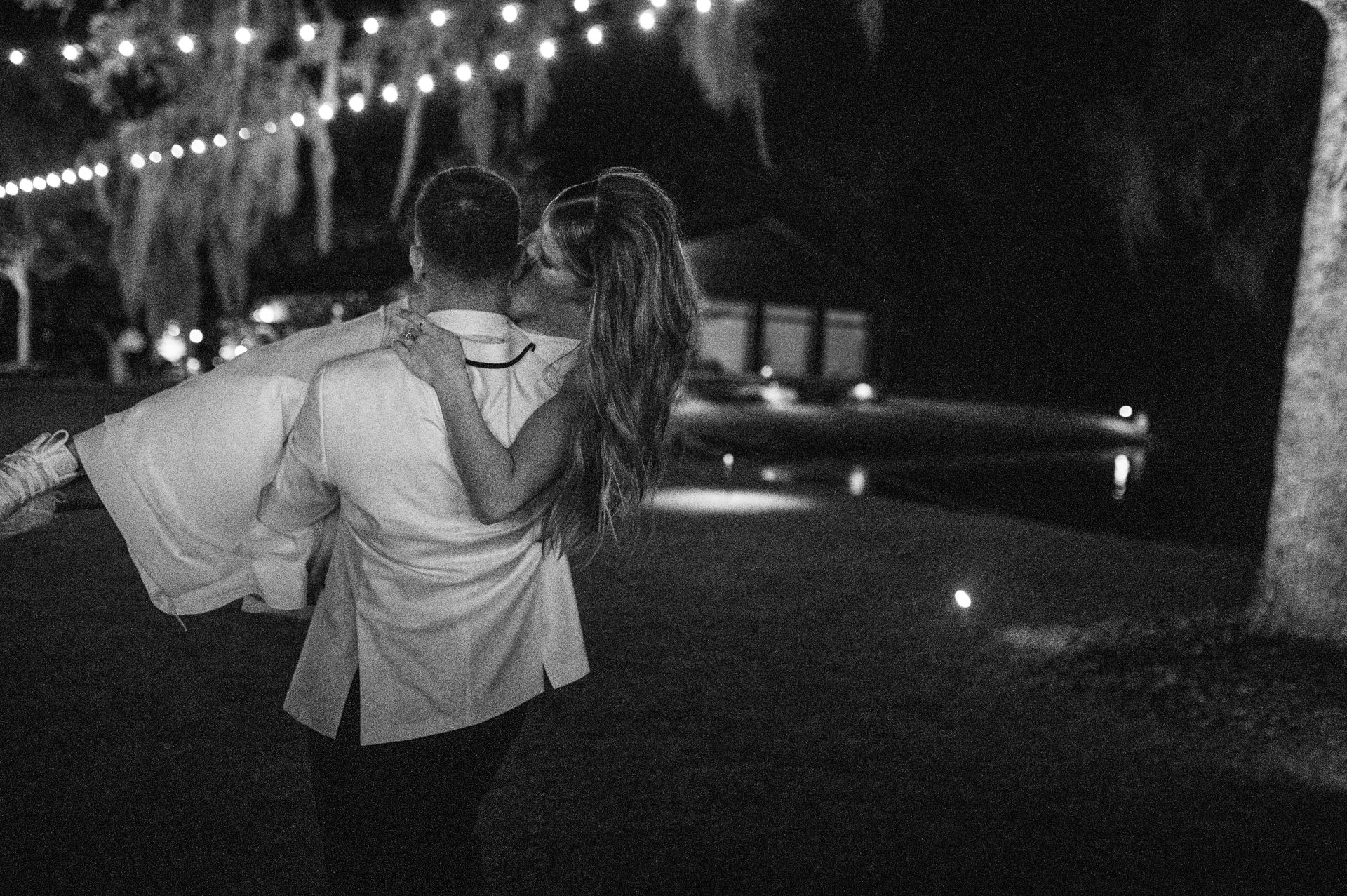 Two people walking at night on a lit sidewalk, one with an arm around the other.