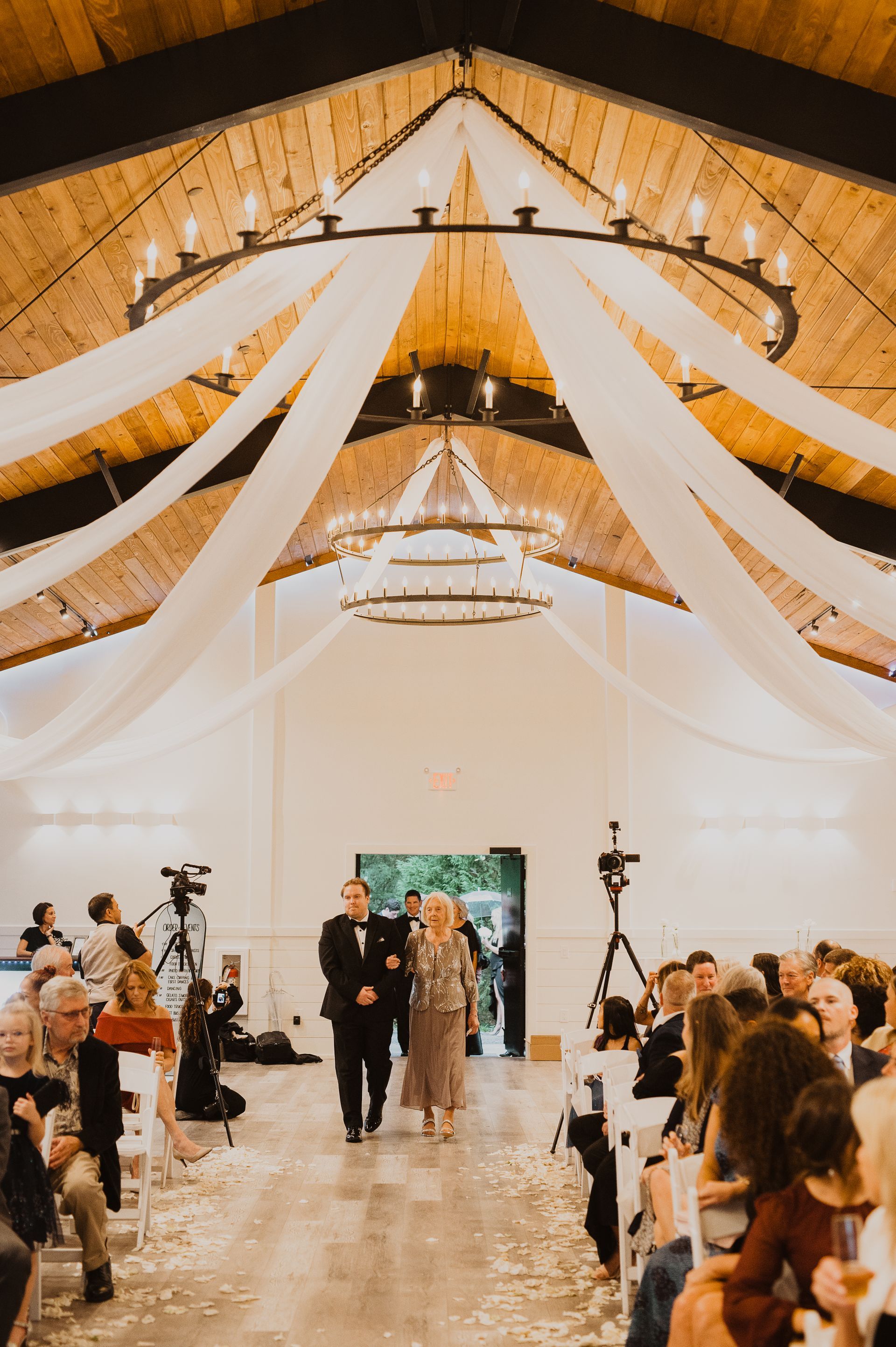 Wedding ceremony in a white-draped hall with guests seated along a central aisle