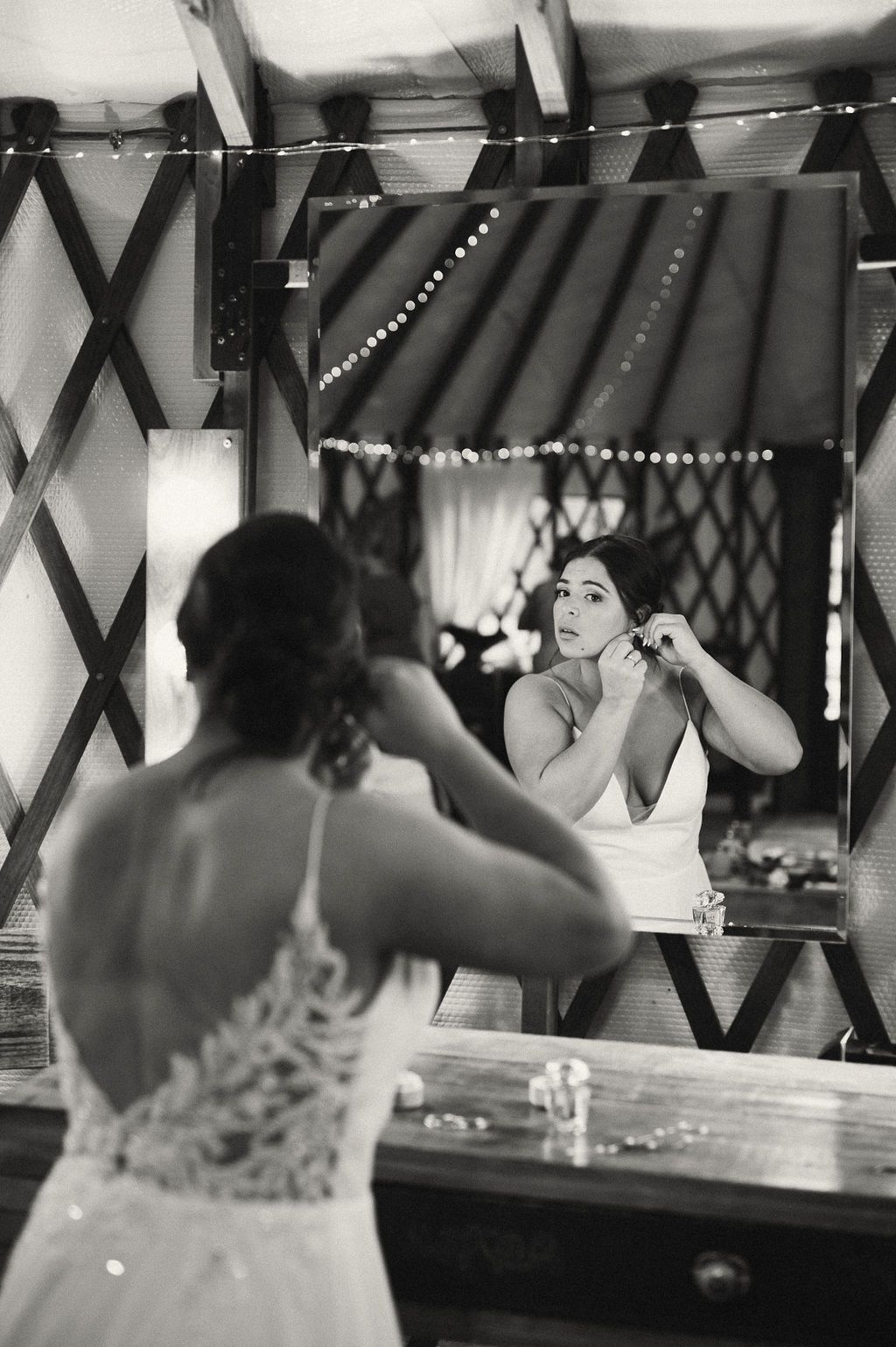 Woman in a white dress adjusting her hair in a mirror above a bathroom sink.