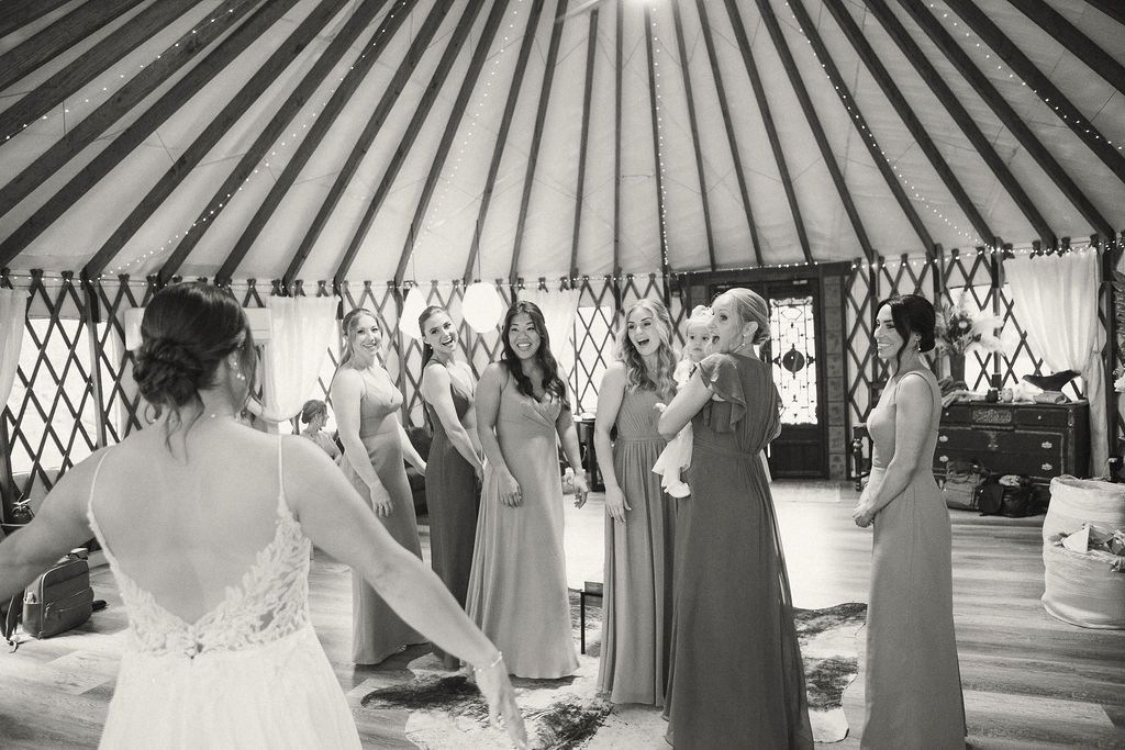 Women in dresses standing inside a striped tent, facing a bride in the foreground