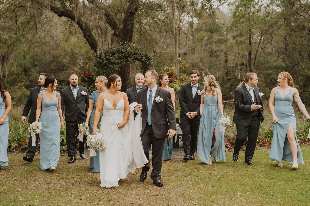 Wedding party walking outdoors in a wooded park, with the bride and groom centered among attendants.