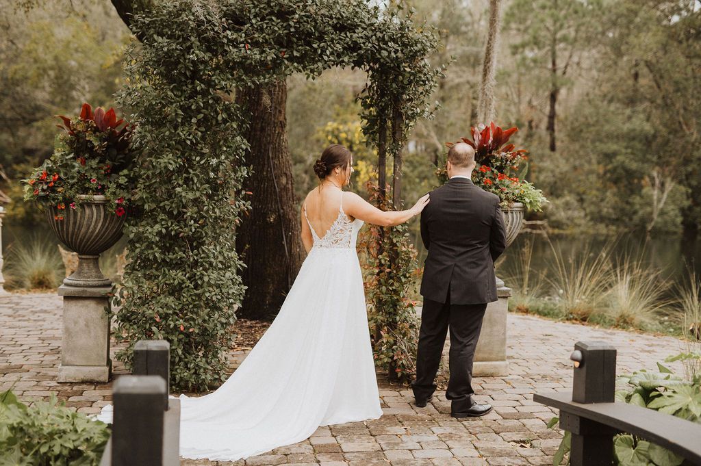 Bride in white gown and groom in black suit stand on a garden path during an outdoor wedding ceremony