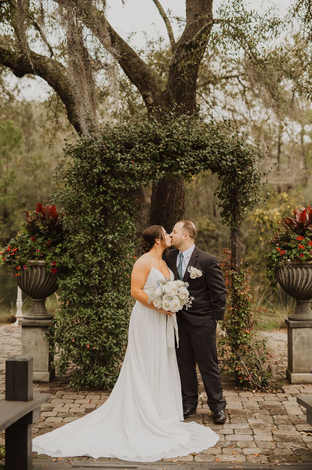 Bride and groom kissing under a floral arch in an outdoor garden setting