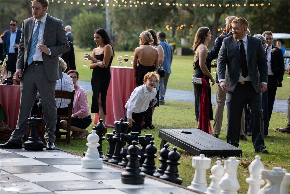 People gathered around a giant outdoor chessboard in a park, with oversized black and white pieces.