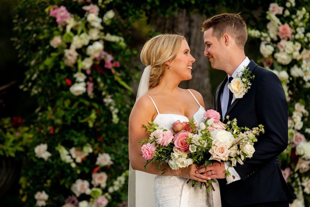 Newlyweds smiling and holding bouquets in front of a floral backdrop
