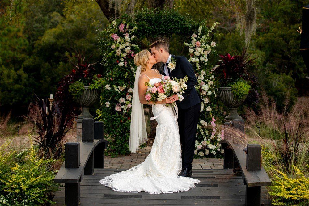Bride and groom kissing at an outdoor wedding altar with floral arrangements and greenery.