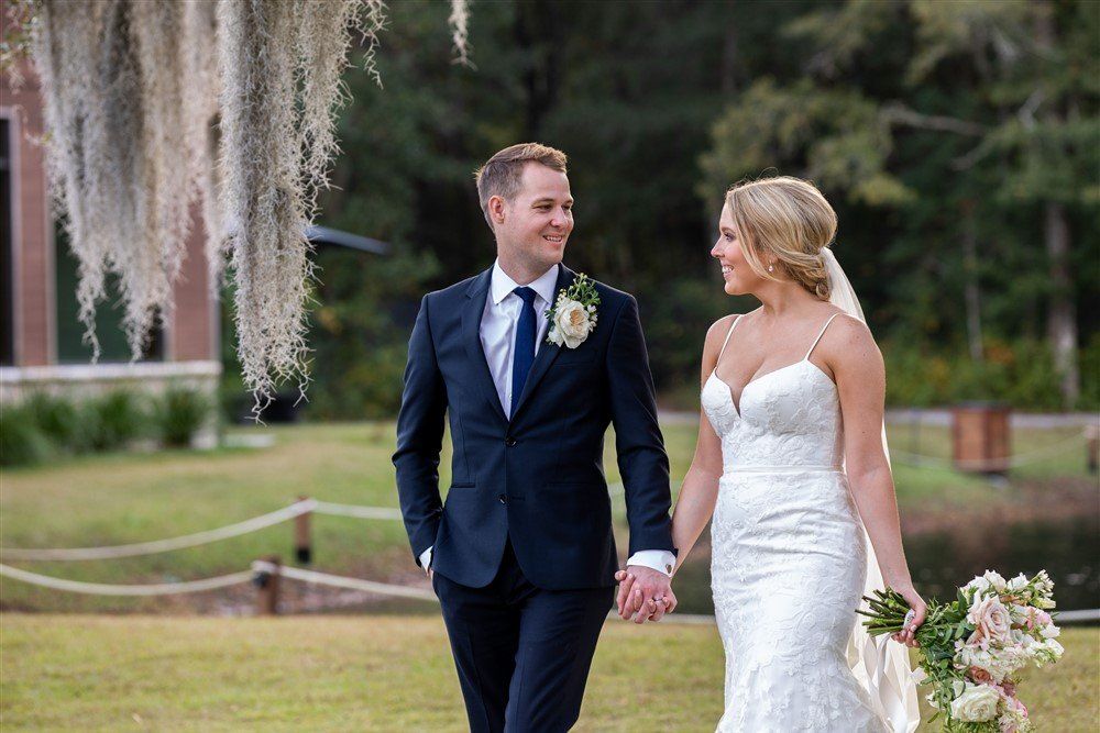 Bride and groom in formal attire holding hands in a garden, smiling at each other
