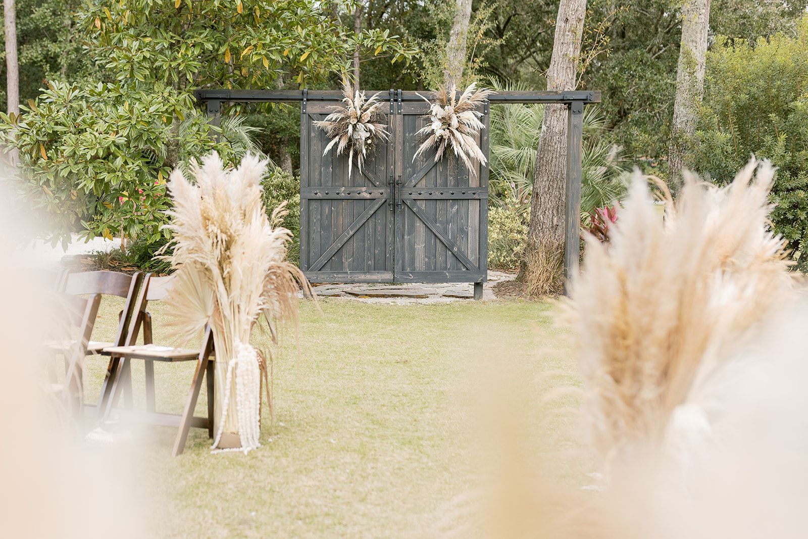 Rustic outdoor wedding backdrop with black double doors, pampas grass arrangements, and greenery
