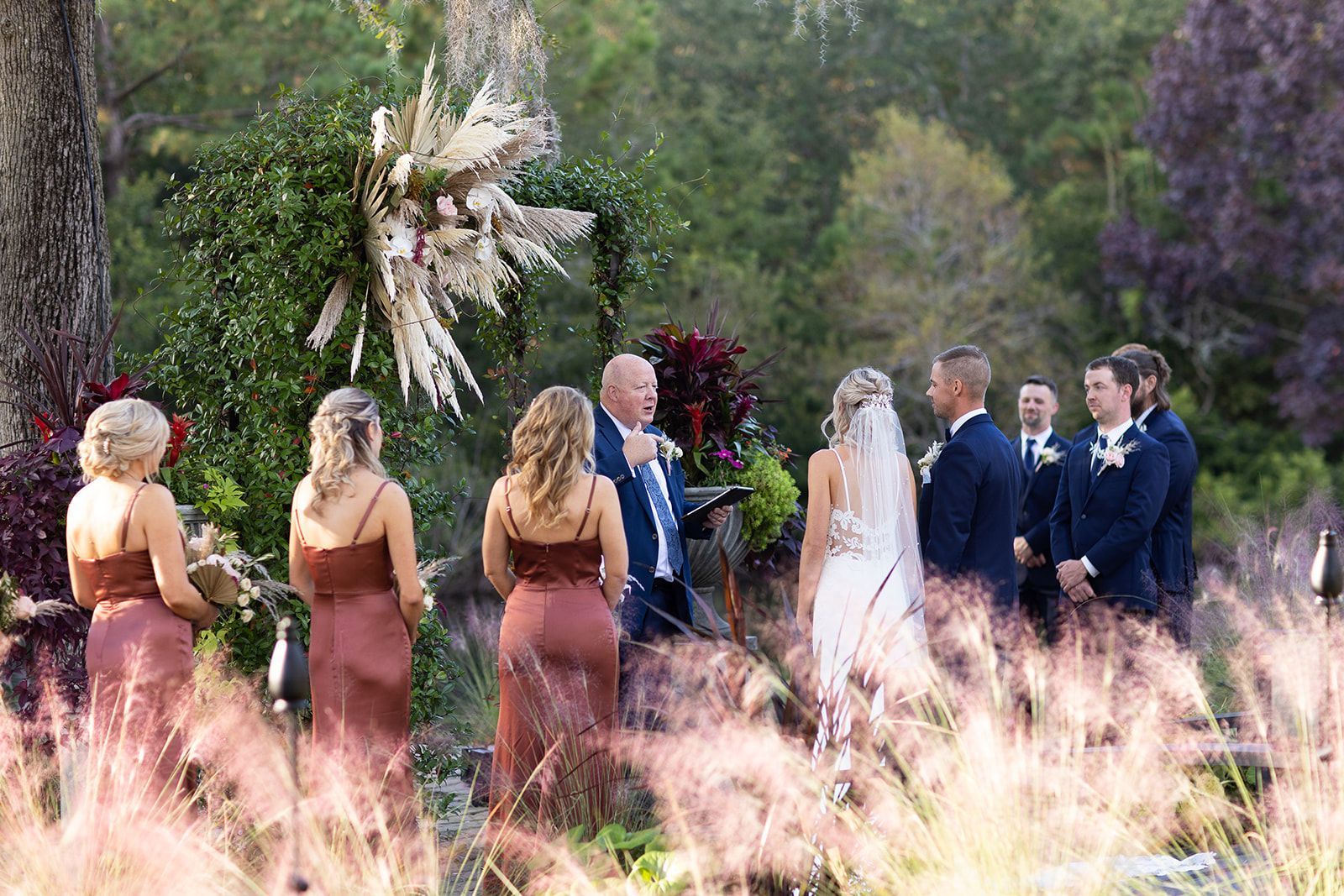 Wedding party standing outdoors in a garden, with the bride and groom at the center.