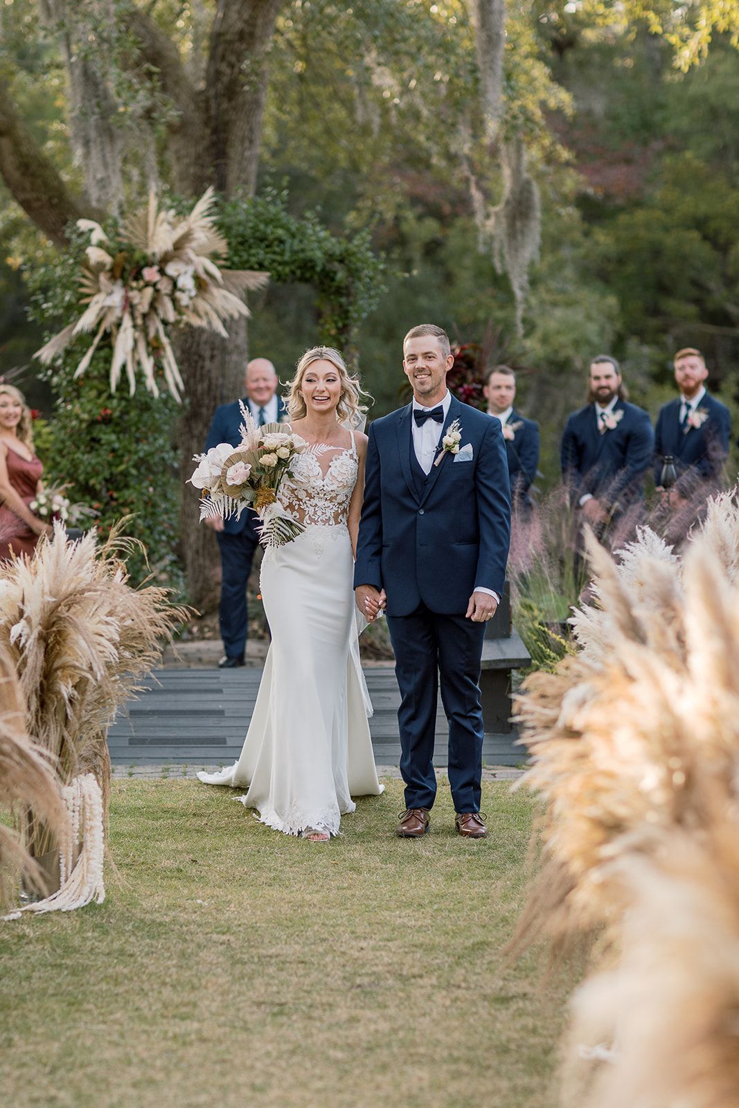 Wedding couple standing at the altar outdoors, surrounded by flowers and guests.