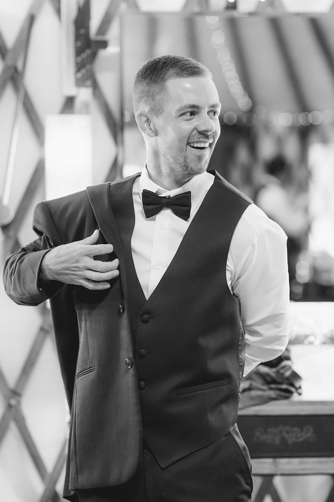 Man in a vest and bow tie smiling while adjusting a jacket indoors