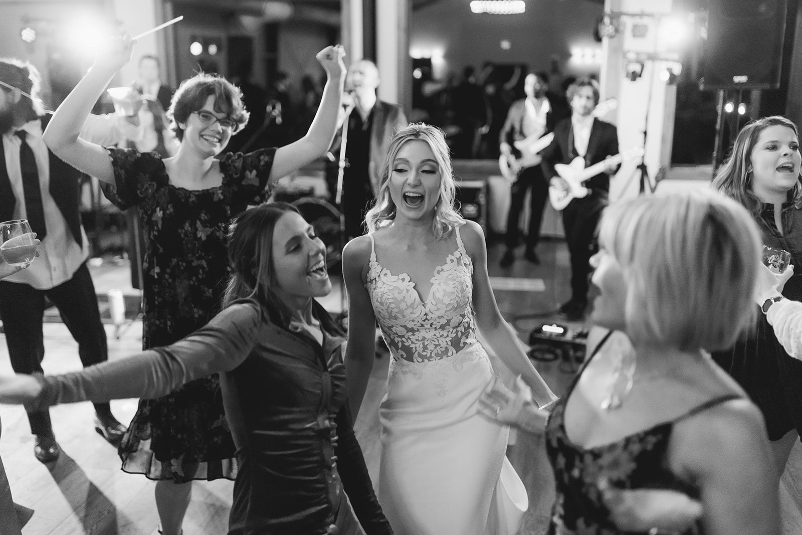 Guests dancing at a lively black-and-white wedding reception, with people smiling and raising their arms.