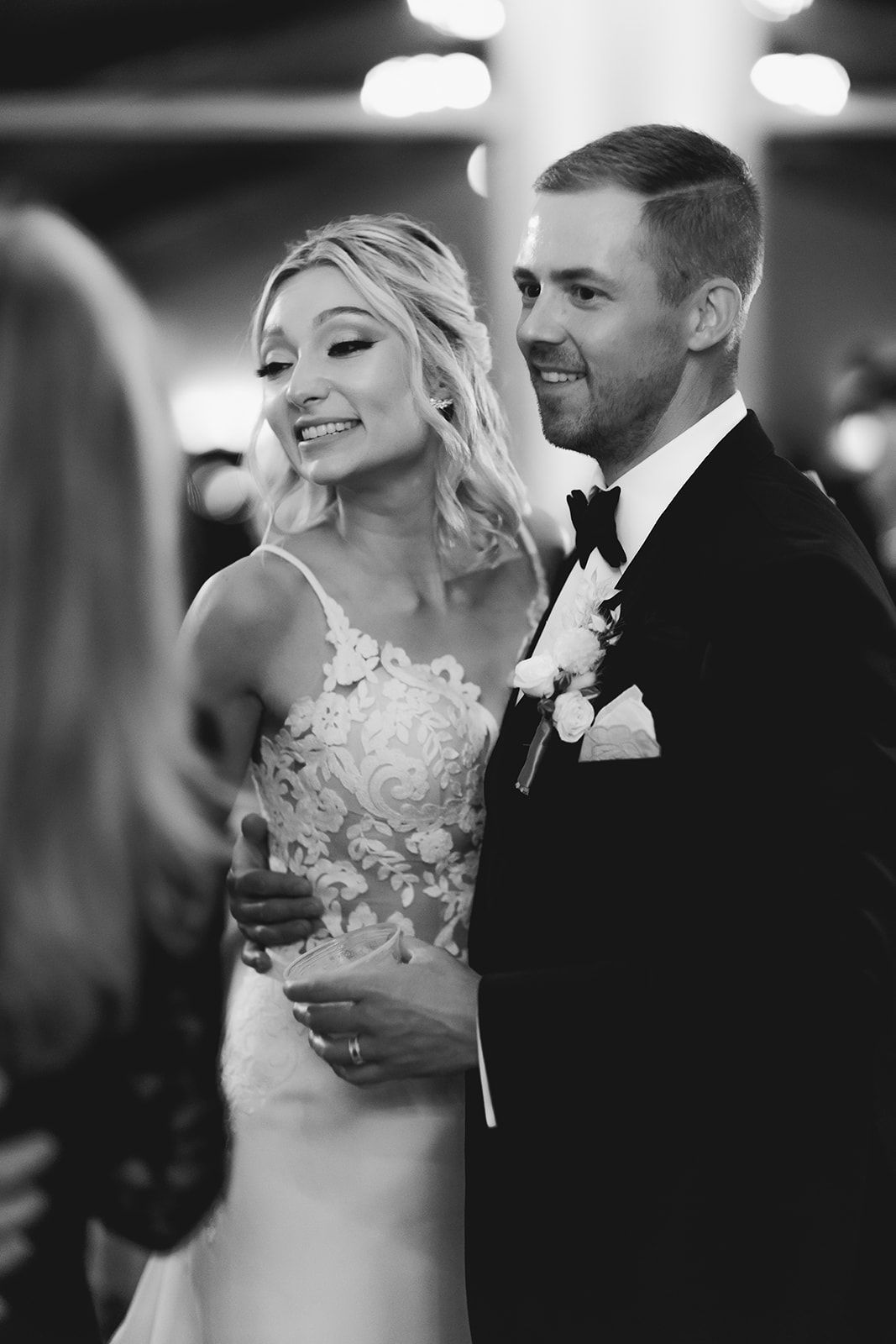 Bride and groom smiling at a wedding reception, dressed in formal black and white attire.