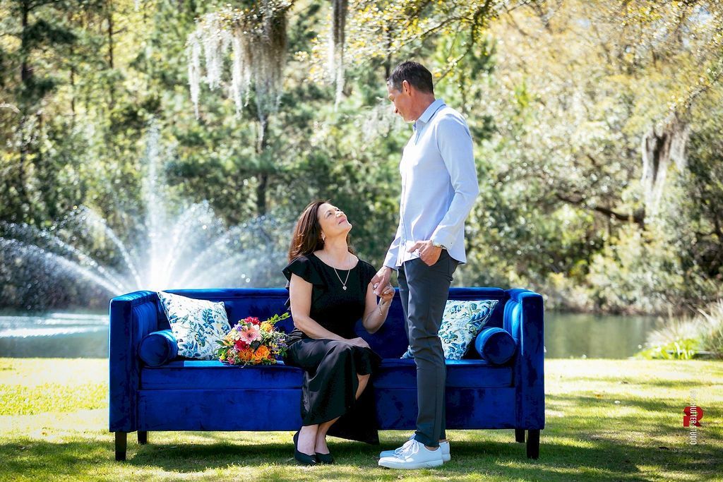 Couple on blue couch in sunny park, holding hands by fountain and flowers