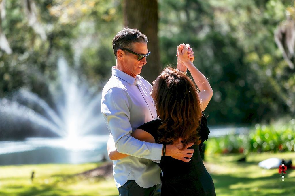 Couple dancing in a park, with a fountain spraying in the background.