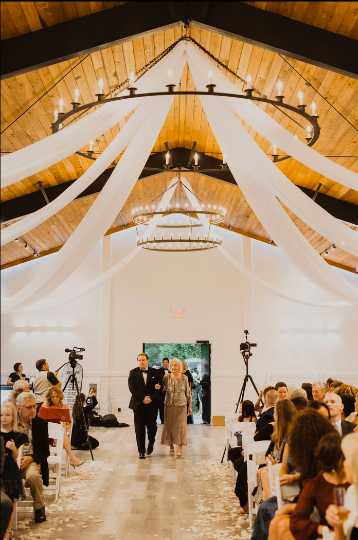 Wedding ceremony in a white decorated hall with draped fabric and guests seated on both sides