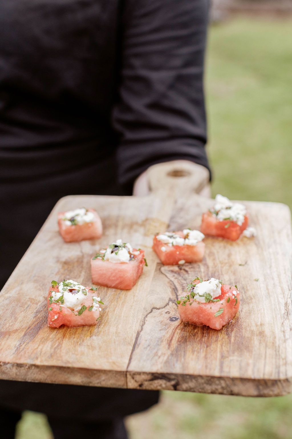 Small salmon appetizers topped with herbs on a wooden board held outdoors