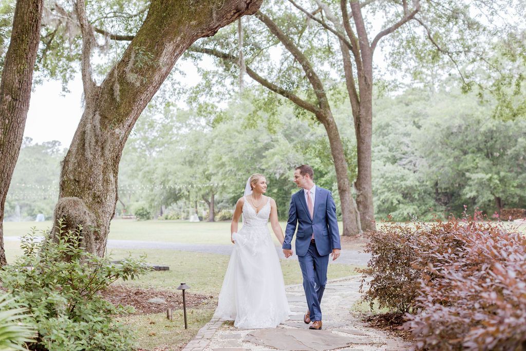 Bride and groom walking hand in hand along a garden path under trees