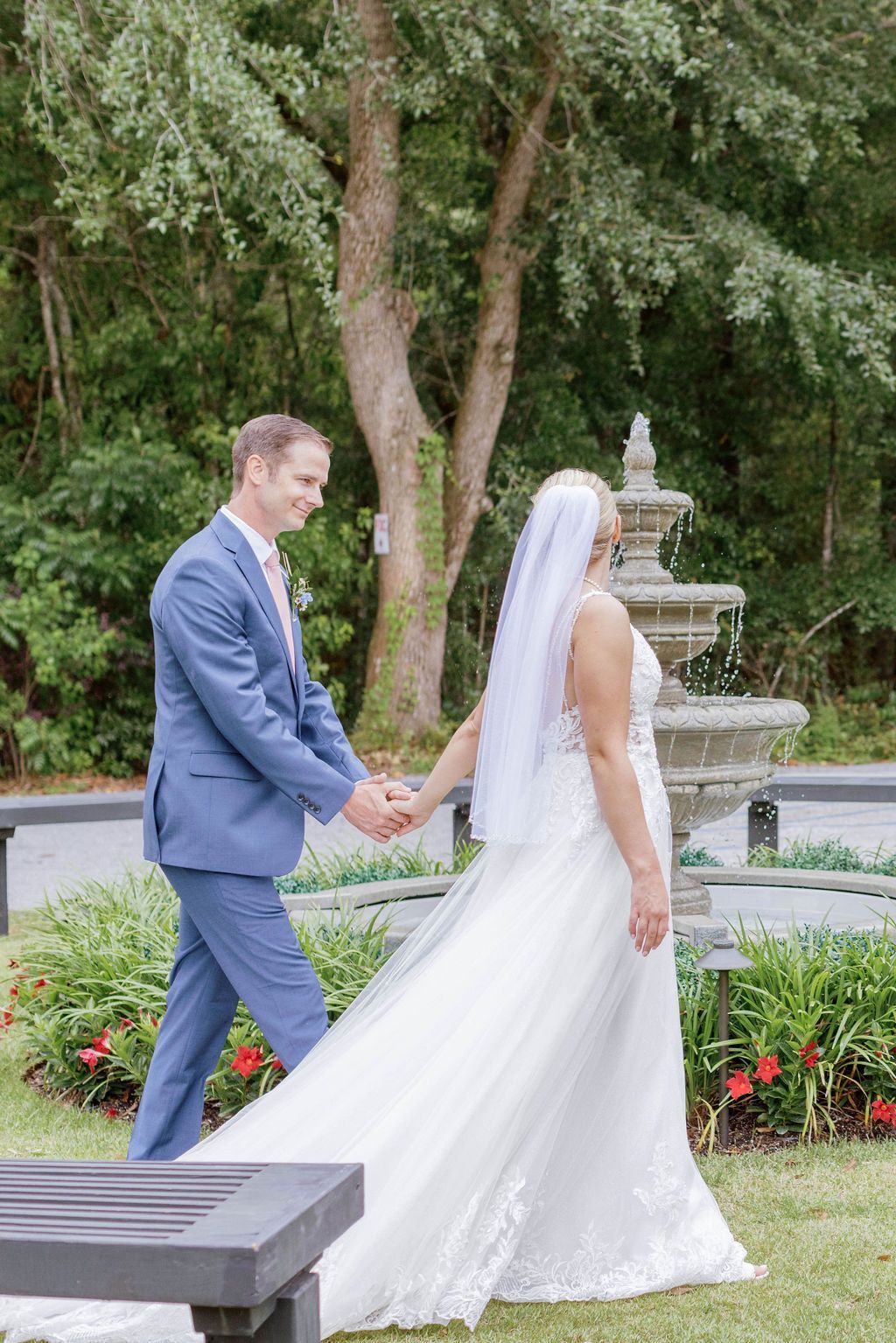 Bride and groom walking hand in hand in a garden near a fountain