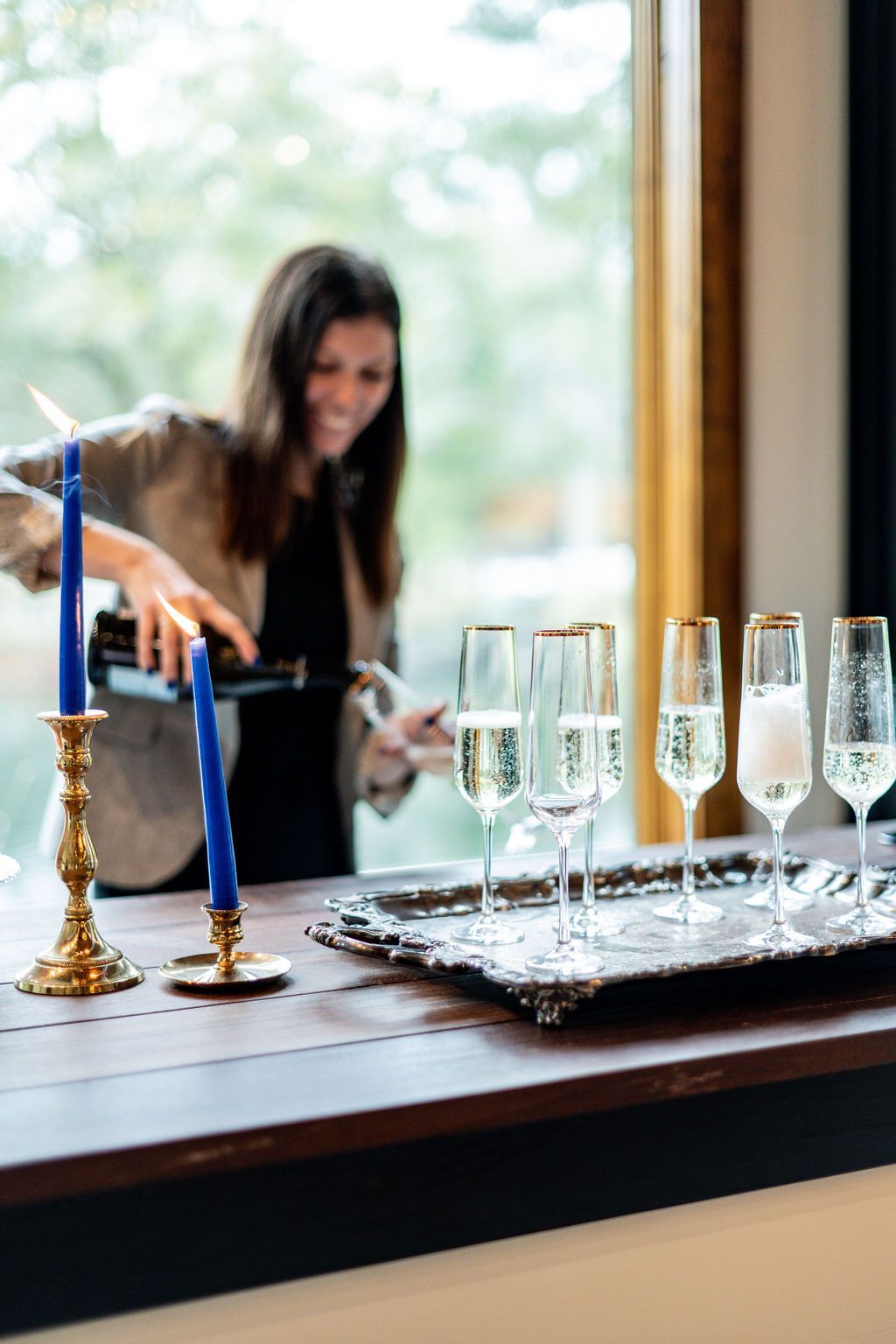 Candles and champagne flutes on a table while a woman arranges them in a bright room