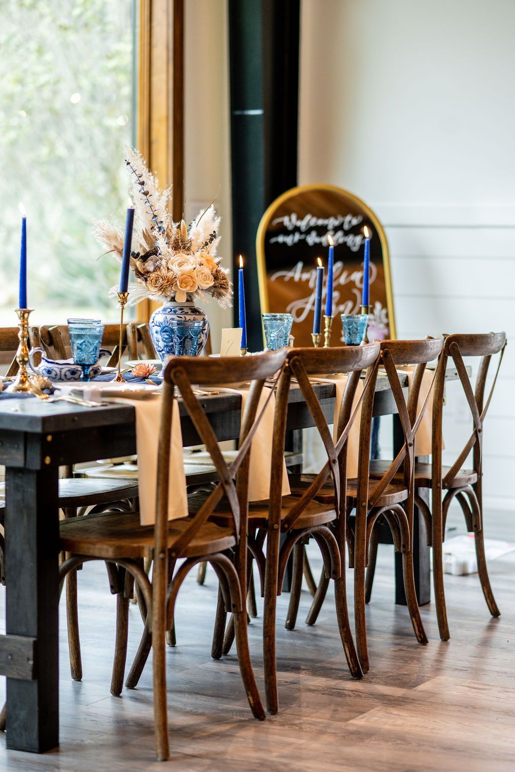 Elegant dining table set with wooden chairs, blue candles, and floral centerpieces in a bright room