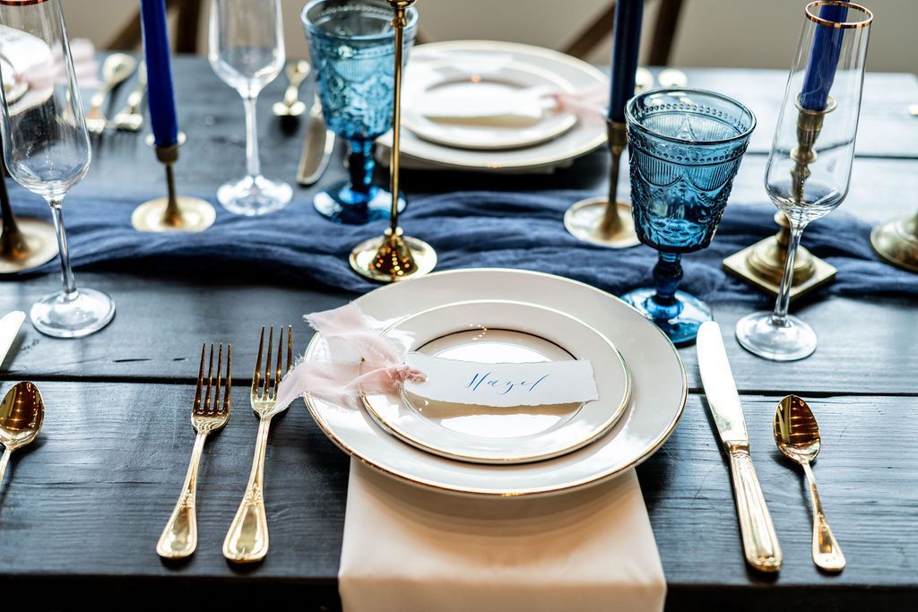 Elegant table setting with blue glassware, gold cutlery, white plates, and folded napkins